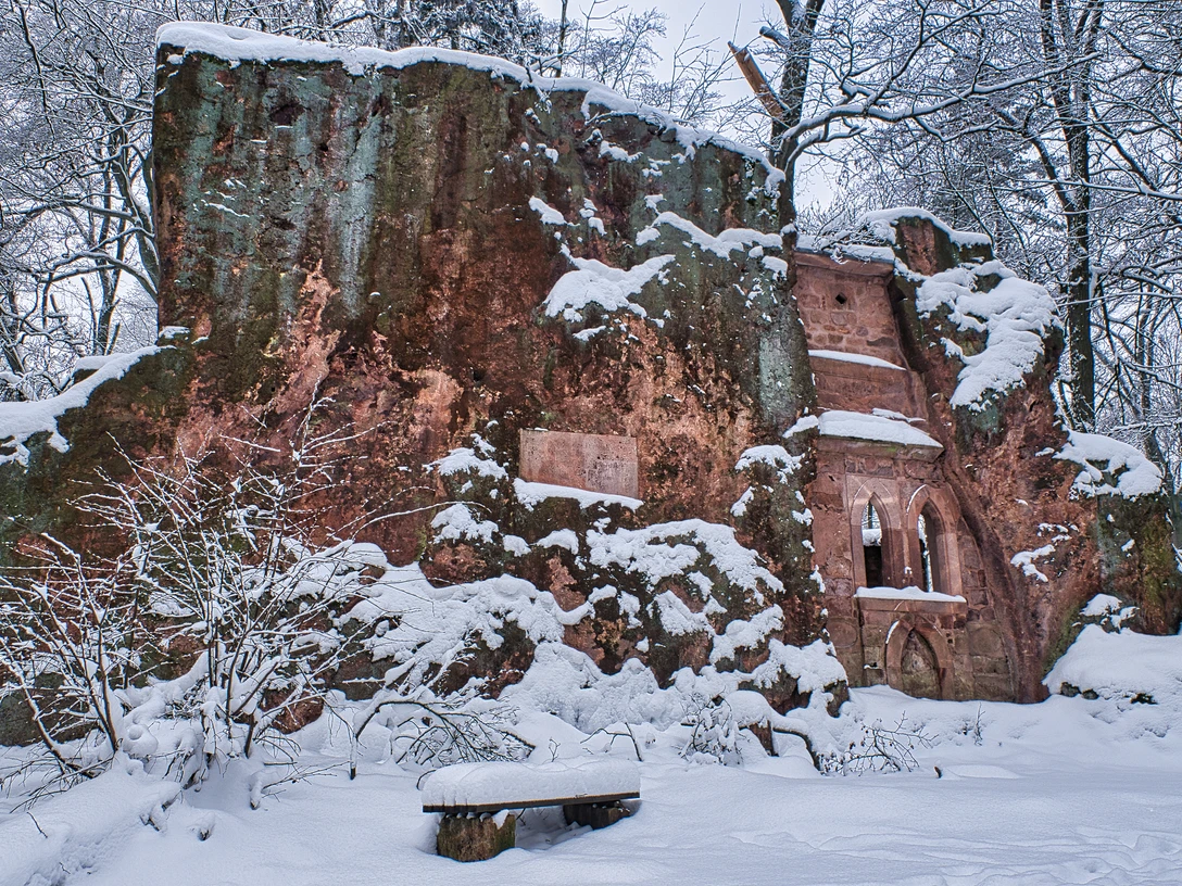 Rochlitzer Berg_Winter_(c)Bastian Rakow_CC BY-SA (6).jpg Zu sehen ist die Einsiedelei, eine Art Wand aus Rochlitzer Porphyrtuff auf dem Rochlitzer Berg. Es liegt Schnee.
