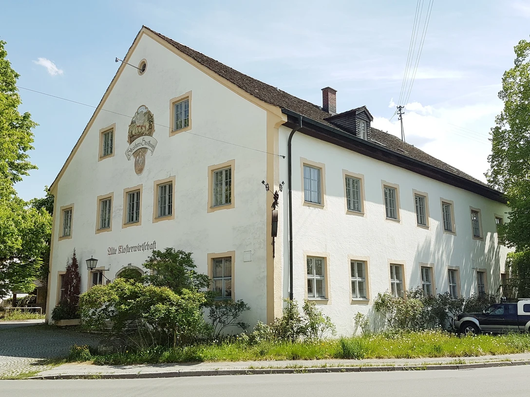 Klosterwirtschaft Polling Großes historisches Haus mit weißer Fassade. Heller Tag. Bäume umgeben das Gebäude.