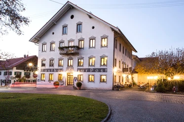 Gasthof zur Post Außen Großes Haus mit vielen Fenstern und warmem Licht am Abend.