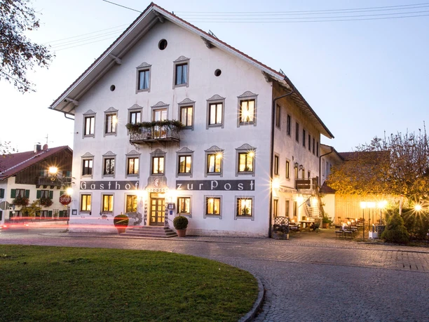 Gasthof zur Post Außen Großes Haus mit vielen Fenstern und warmem Licht am Abend.