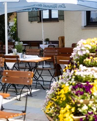 Gasthof zur Post Biergarten Holztische stehen unter Schirmen. Bunte Blumen stehen vorne. Gäste genießen hier Ruhe.