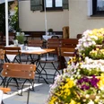 Gasthof zur Post Biergarten Holztische stehen unter Schirmen. Bunte Blumen stehen vorne. Gäste genießen hier Ruhe.