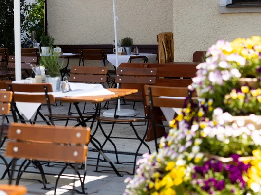 Gasthof zur Post Biergarten Holztische stehen unter Schirmen. Bunte Blumen stehen vorne. Gäste genießen hier Ruhe.