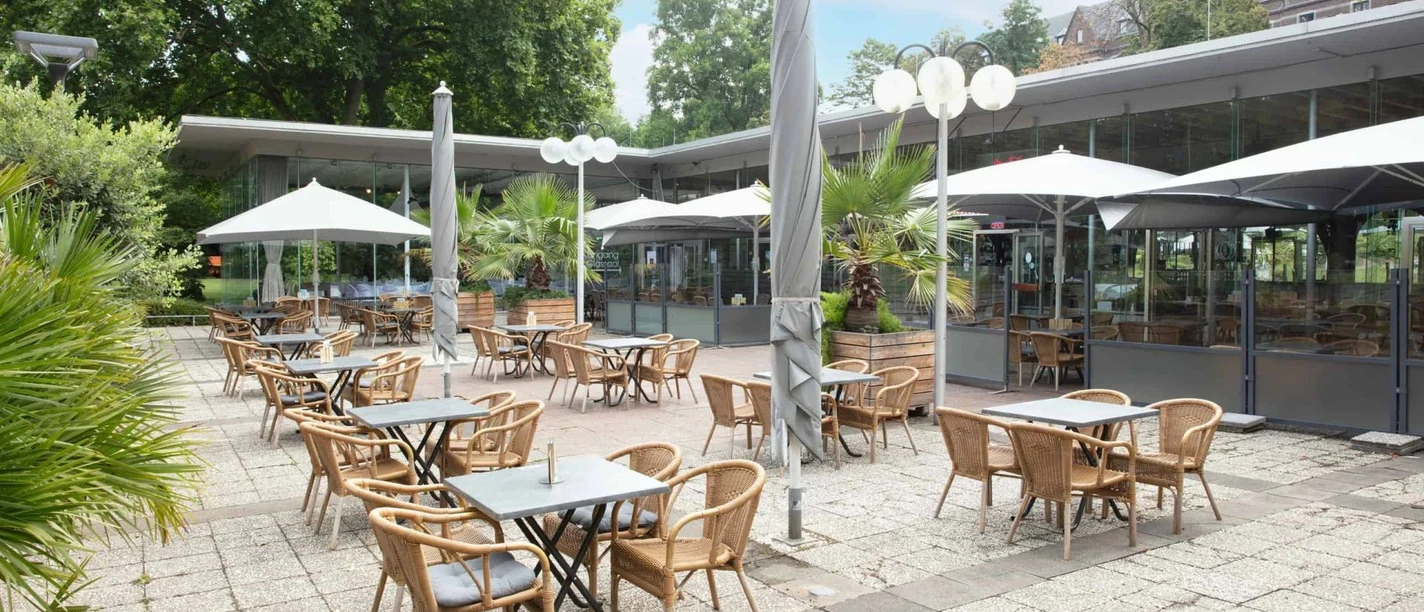 Große Außenterrasse mit vielen Sitzgruppen und Sonnenschirmen, umgeben von Pflanzen in Blumentöpfen.
