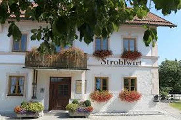 Stroblwirt Weißes Haus mit vielen Blumen und dem Schriftzug Stroblwirt unter grünen Blättern.