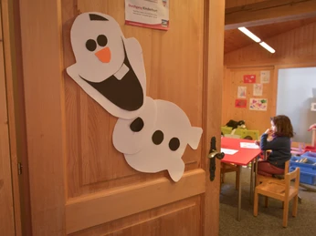Entrée de la garderie Porte d'entrée de la garderie de Fiescheralp avec un bonhomme de neige bricolé et vue sur la salle décorée avec amour