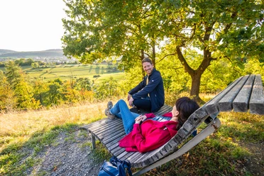 willebadessen-schmetterlingspfad-teutoburger-wald-tourismus-d-ketz-093-jpg.jpg Ein Mann und eine Frau sitzen auf einer Holzliege im Hintergrund eine schöne grüne Aussicht,