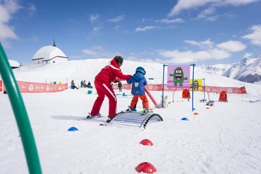 Apprendre à skier en s'amusant Un enfant apprend à skier de manière ludique au Snowgarden Bettmeralp avec le soutien d'un moniteur de ski