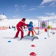 Spielerisch Skifahren lernen Kind lernt im Snowgarden Bettmeralp mit Unterstützung einer Skilehrperson spielerisch SkifahrenChild learns to ski in a playful way at Snowgarden Bettmeralp with the support of a ski instructorUn enfant apprend à skier de manière ludique au Snowgarden Bettmeralp avec le soutien d'un moniteur de ski