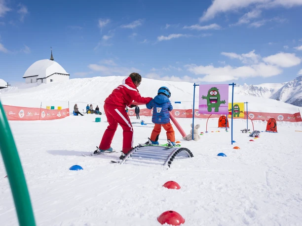 Spielerisch Skifahren lernen Kind lernt im Snowgarden Bettmeralp mit Unterstützung einer Skilehrperson spielerisch Skifahren