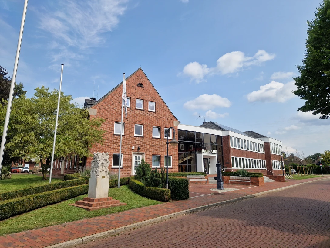 Rathaus der Gemeinde Schwanewede Backsteingebäude des Rathauses Schwanewede mit gepflegtem Vorplatz, Flaggenmasten und Skulptur.
