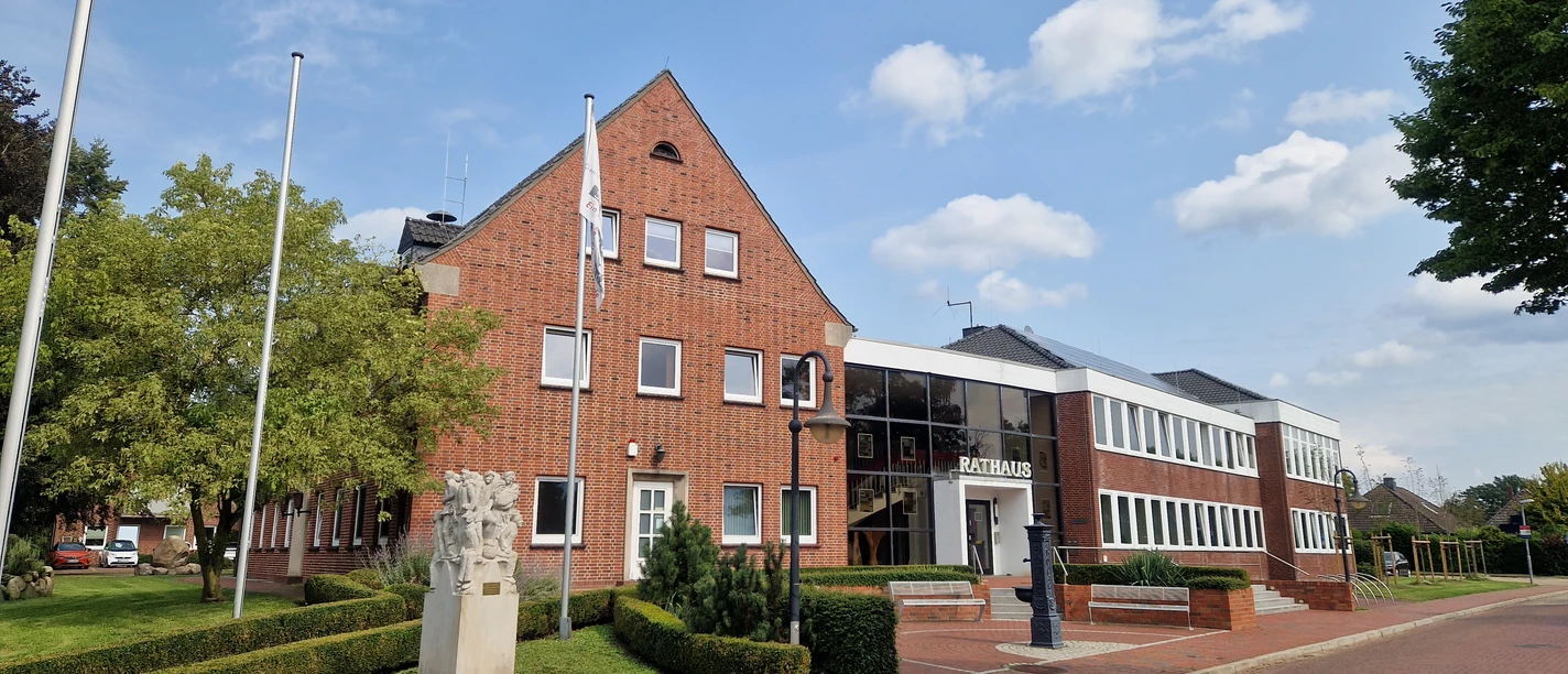 Rathaus der Gemeinde Schwanewede Backsteingebäude des Rathauses Schwanewede mit gepflegtem Vorplatz, Flaggenmasten und Skulptur.