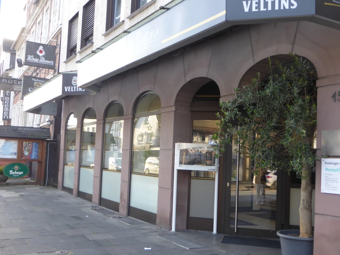 Ronny`s La Casa Straßenansicht des Eingangs von Ronny’s La Casa mit Arkaden, Werbeschild und Pflanze.