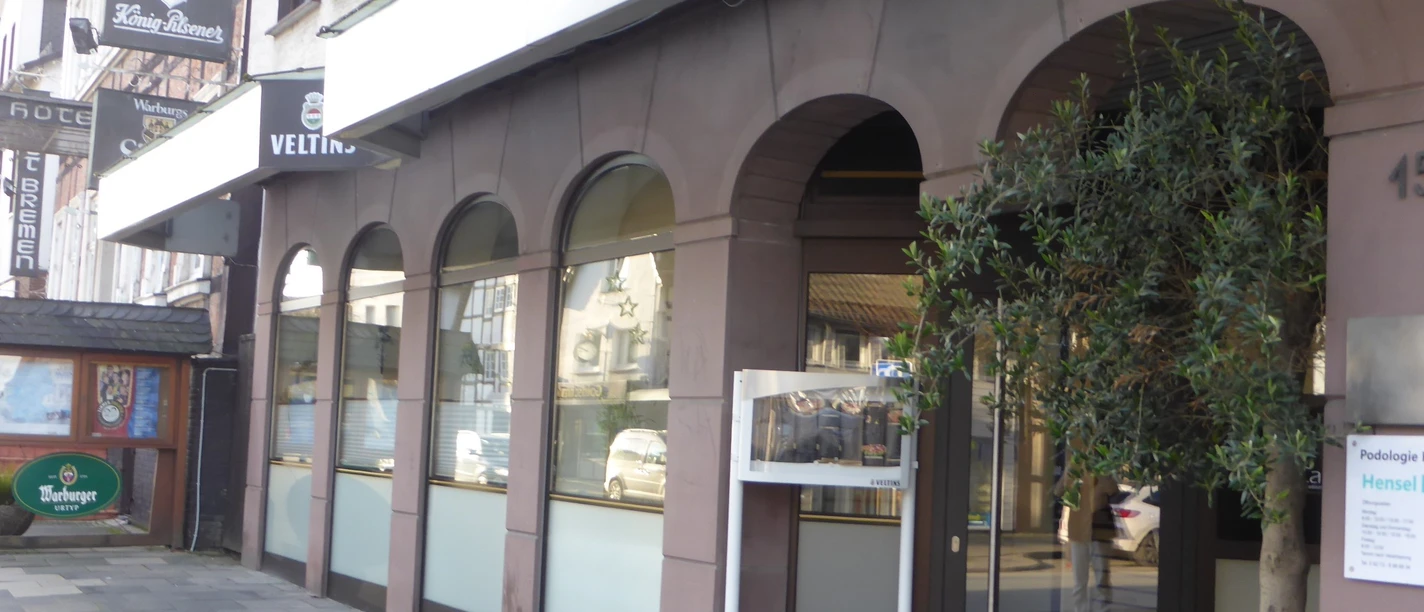 Ronny`s La Casa Straßenansicht des Eingangs von Ronny’s La Casa mit Arkaden, Werbeschild und Pflanze.