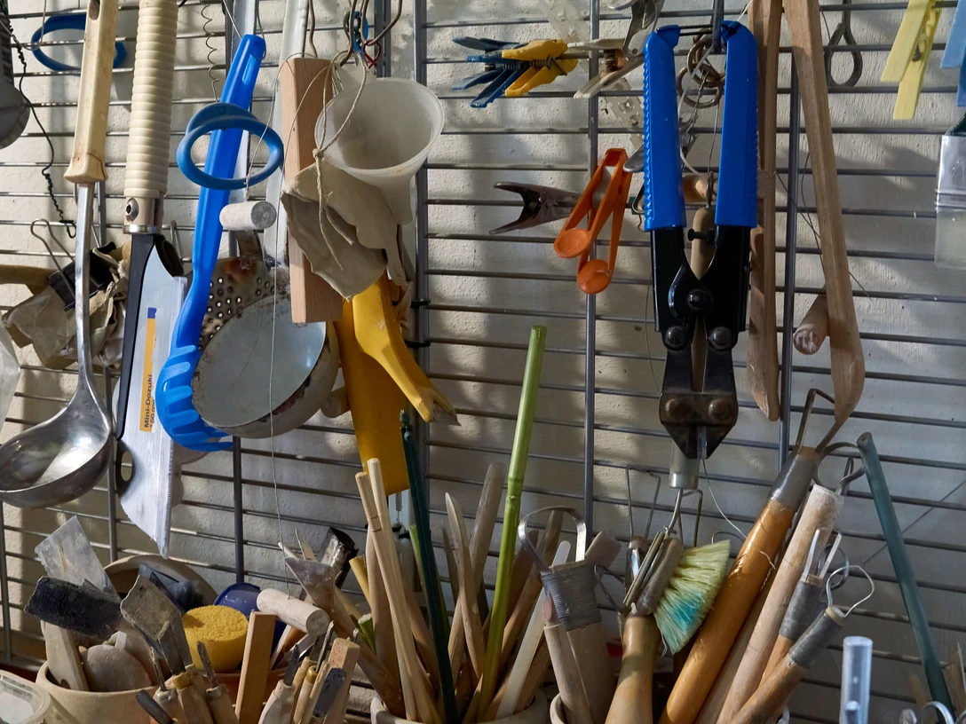 Keramikwerkzeug Verschiedene Küchenutensilien und Werkzeuge an einer Wand und in Behältern.