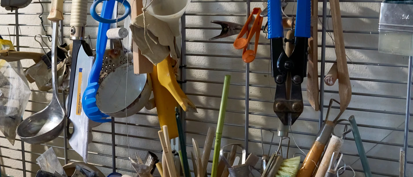 Keramikwerkzeug Verschiedene Küchenutensilien und Werkzeuge an einer Wand und in Behältern.