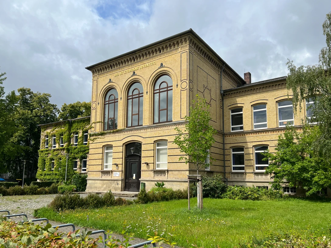 Große_Schule.jpg Historisches Schulgebäude aus gelbem Klinker mit großen Rundbogenfenstern und begrünter Fassade.