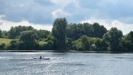 Kanufahren_Salzgittersee_HD_16zu9.JPG Eine Person im blauen Kanu paddelt auf dem glitzernden Salzgittersee vor dicht bewaldetem Ufer.