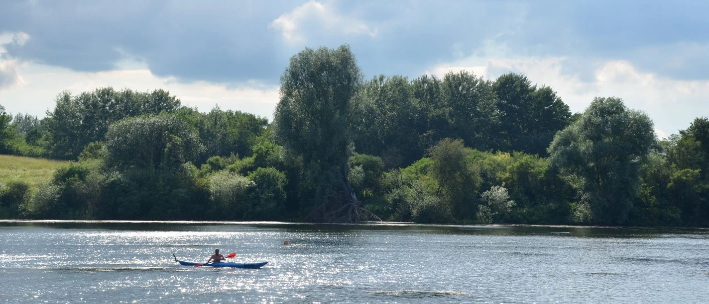 Kanufahren_Salzgittersee_HD_16zu9.JPG Eine Person im blauen Kanu paddelt auf dem glitzernden Salzgittersee vor dicht bewaldetem Ufer.