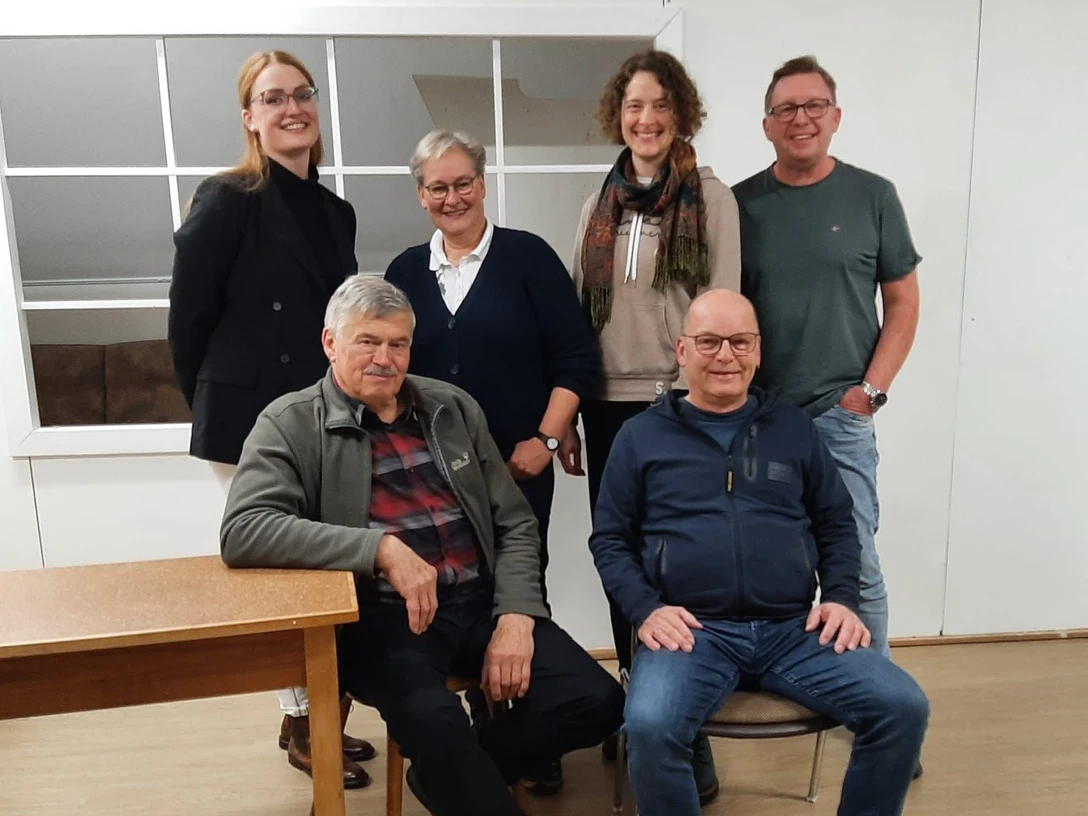 Gruppenbild SPKW ohne Namen.jpg Sechs Personen stehen und sitzen in einem Raum. Sie lächeln freundlich in die Kamera.