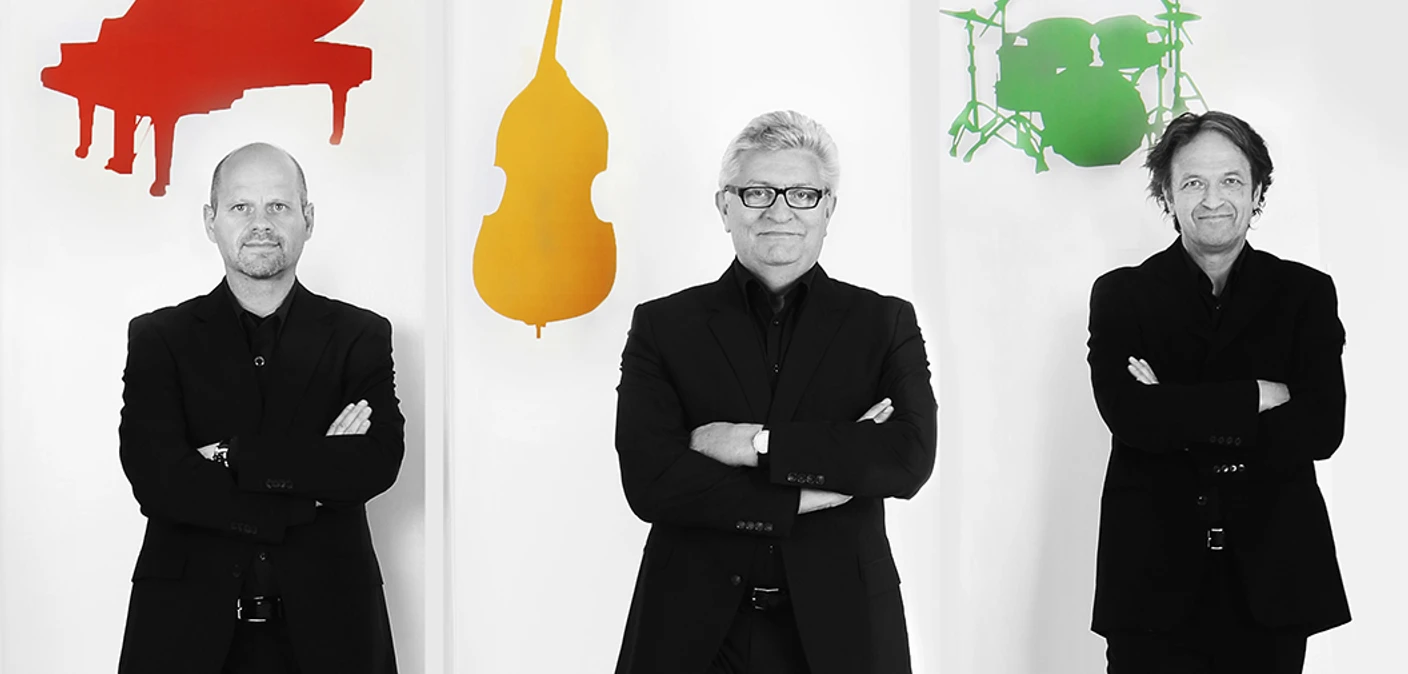 KTG Trio Drei Musiker in Schwarz vor farbigen Silhouetten von Flügel, Bass und Schlagzeug.