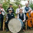 Rootbirds.jpg Sechs Musiker in Vintage-Kleidung mit Banjo, Trompete, Saxofon, Bass und großer Trommel im Freien