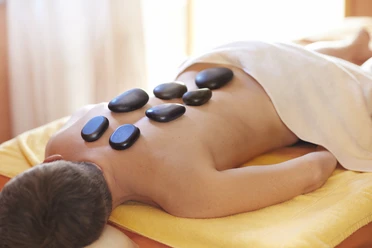 Person liegt auf einer Liege im Wellnessbereich. Auf dem Rücken sind Steine.