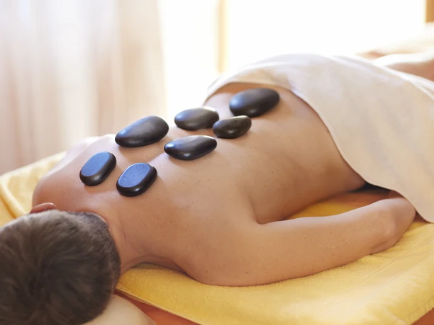Person liegt auf einer Liege im Wellnessbereich. Auf dem Rücken sind Steine.