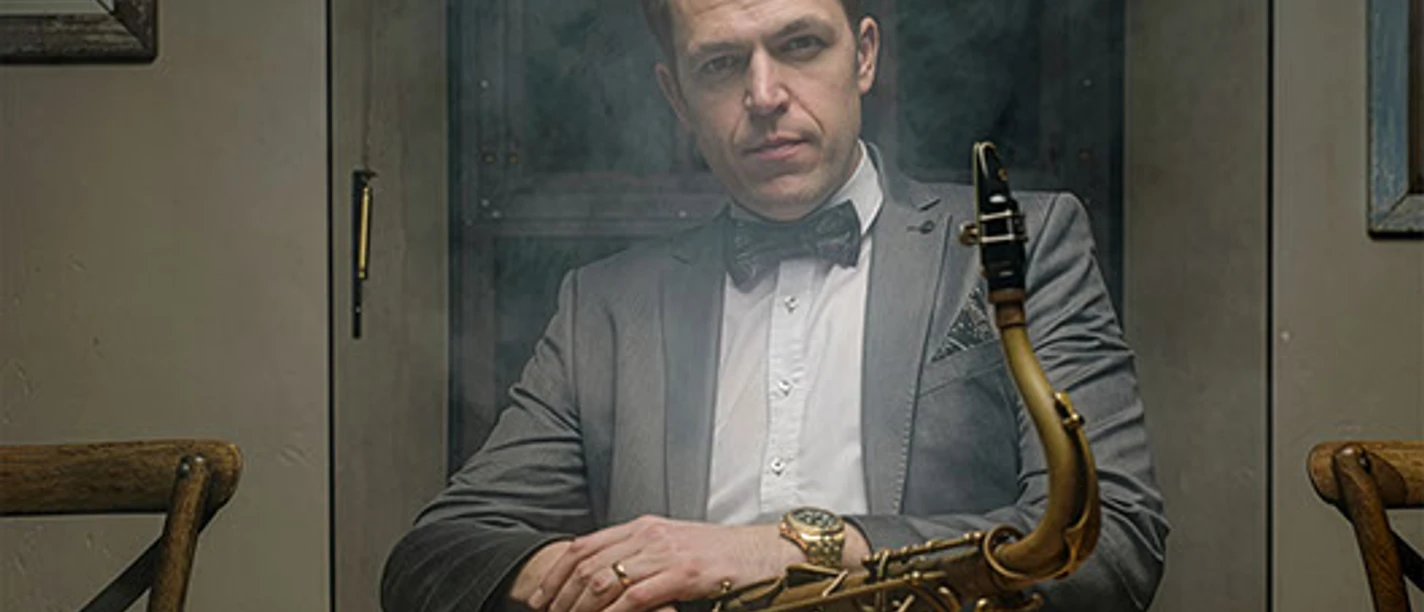 Johannes Müller Quartett Mann in Anzug sitzt rauchumhüllt an Tisch und hält ein Saxofon auf dem Schoß.