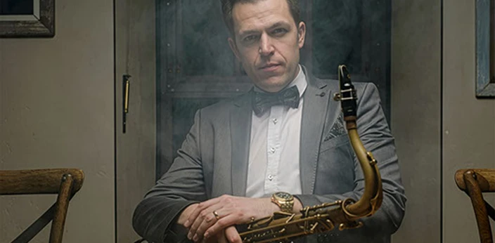 Johannes Müller Quartett Mann in Anzug sitzt rauchumhüllt an Tisch und hält ein Saxofon auf dem Schoß.