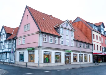 BreiteHerzogstraße.jpg Mehrstöckiges Eckhaus mit roten Ziegeldächern, pastellfarbenen Fassaden und Straßenfront.