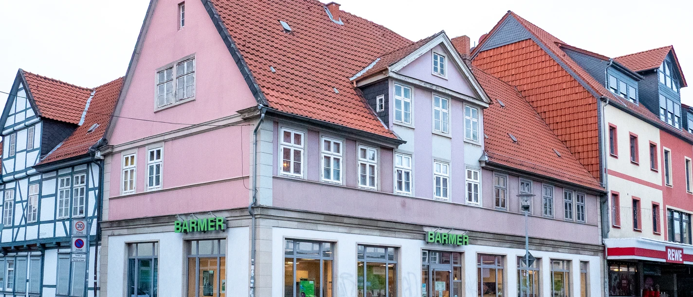 BreiteHerzogstraße.jpg Mehrstöckiges Eckhaus mit roten Ziegeldächern, pastellfarbenen Fassaden und Straßenfront.
