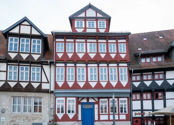 Schlossplatz18.jpg Fachwerkhaus mit roter und weißer Fassade, blauen Türrahmen und zahlreichen Fenstern am Schlossplatz.