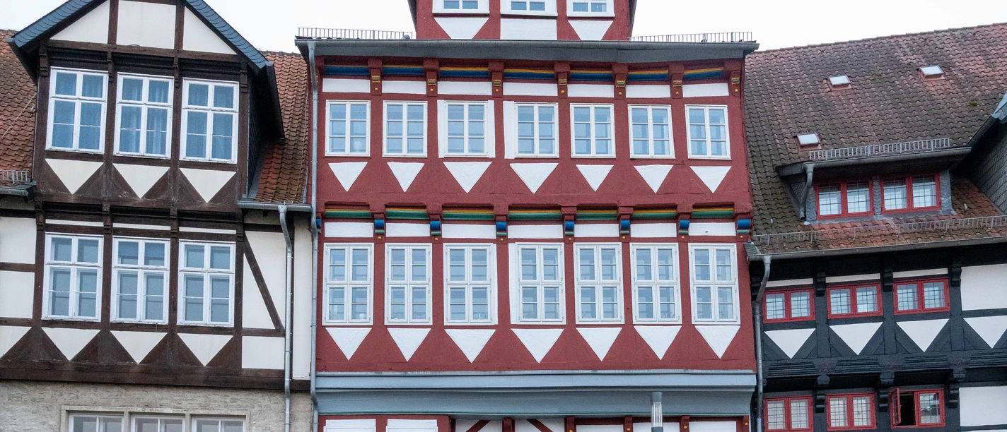 Schlossplatz18.jpg Fachwerkhaus mit roter und weißer Fassade, blauen Türrahmen und zahlreichen Fenstern am Schlossplatz.
