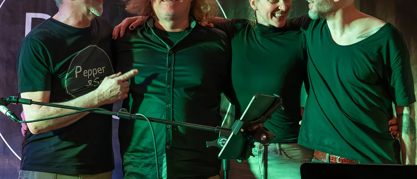 043_Copyright_Sylvia_Bothmer_NWT.png Vier Personen stehen eng beieinander auf einer Bühne, zwei Männer und zwei Frauen, alle tragen dunkle Oberteile, eine Person zeigt mit dem Finger auf eine andere.