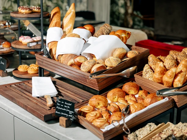 Brunch buffet with fresh bread rolls, baguettes, croissants and pastries in wooden trays