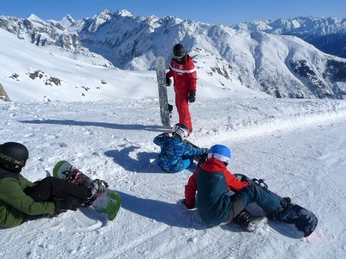 Pause avec vue sur la montagne Kinder sitzen im Snowboard Schnupperkurs Fiescheralp mit Snowboards vor hochalpiner KulisseChildren sit on snowboards in front of a high alpine backdrop on the Fiescheralp snowboard taster courseLes enfants s'assoient dans le cours d'initiation au snowboard de Fiescheralp avec des snowboards dans un décor de haute montagne.