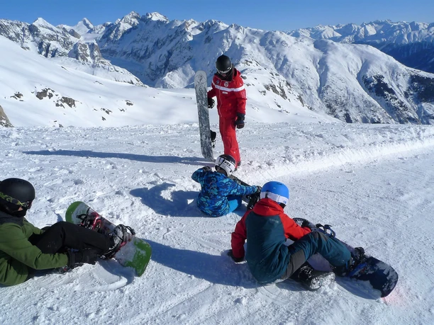 Pause avec vue sur la montagne Les enfants s'assoient dans le cours d'initiation au snowboard de Fiescheralp avec des snowboards dans un décor de haute montagne.