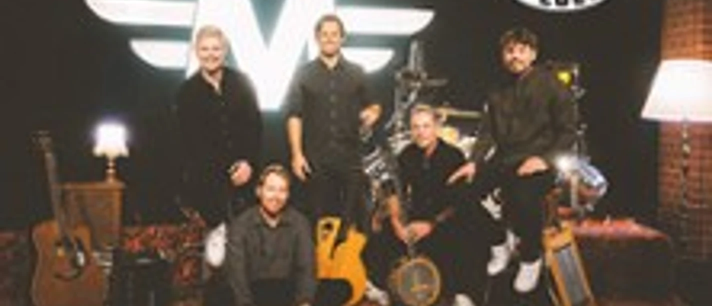 Fünf Musiker sitzen und stehen vor Instrumenten in einem warm beleuchteten Studio mit Miljö-Logo