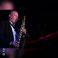 Saxophonist im dunklen Anzug spielt beleuchtet auf einer Bühne im Club