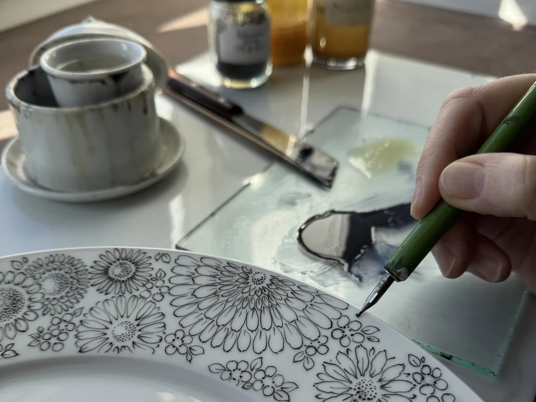 VHS-Filigrane Dekor_Federzeichnungen.jpg Weißer Teller wird von einer Fabfeder mit Ornamenten verziert