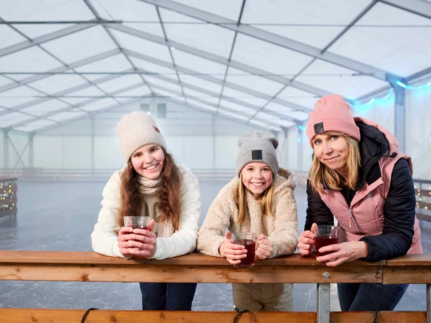 Drei Frauen in Winterkleidung lehnen an einer Brüstung und halten Becher.