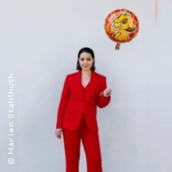 Frau im roten Anzug vor weißer Wand hält bunten Luftballon mit Tiermotiv.