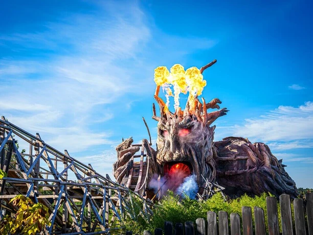 heide-park-resort-soltau-biest-colossos.jpg Feuerspeiendes Colossos-Holzachterbahn-Monster im Heide Park Soltau Resort unter blauem Himmel.