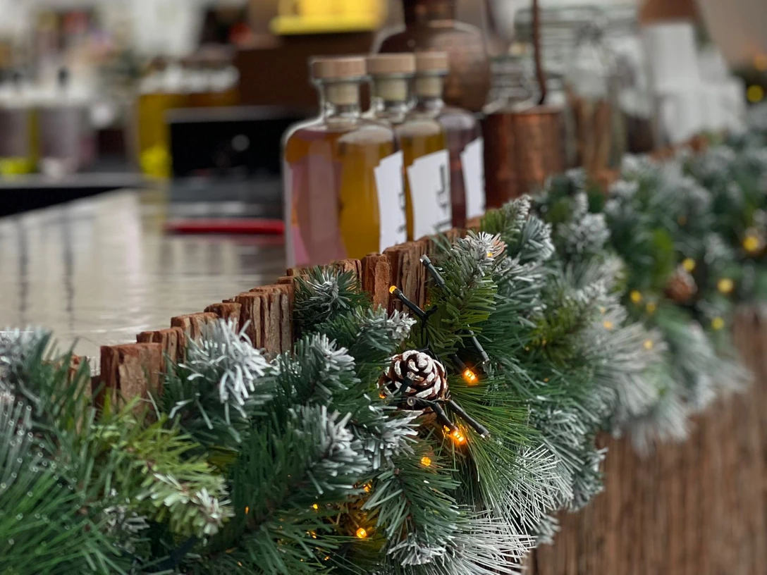 X-mas Markets Tour Weihnachtsmarktstand mit Lichtergirlande, Tannenzweigen und Flaschen auf dem TresenChristmas market stall with garland of lights, fir branches and bottles on the counter