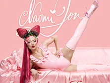 Person mit rosa Outfit und Erdbeer-Kopfschmuck posiert auf rosa Stoff vor Tourtitel