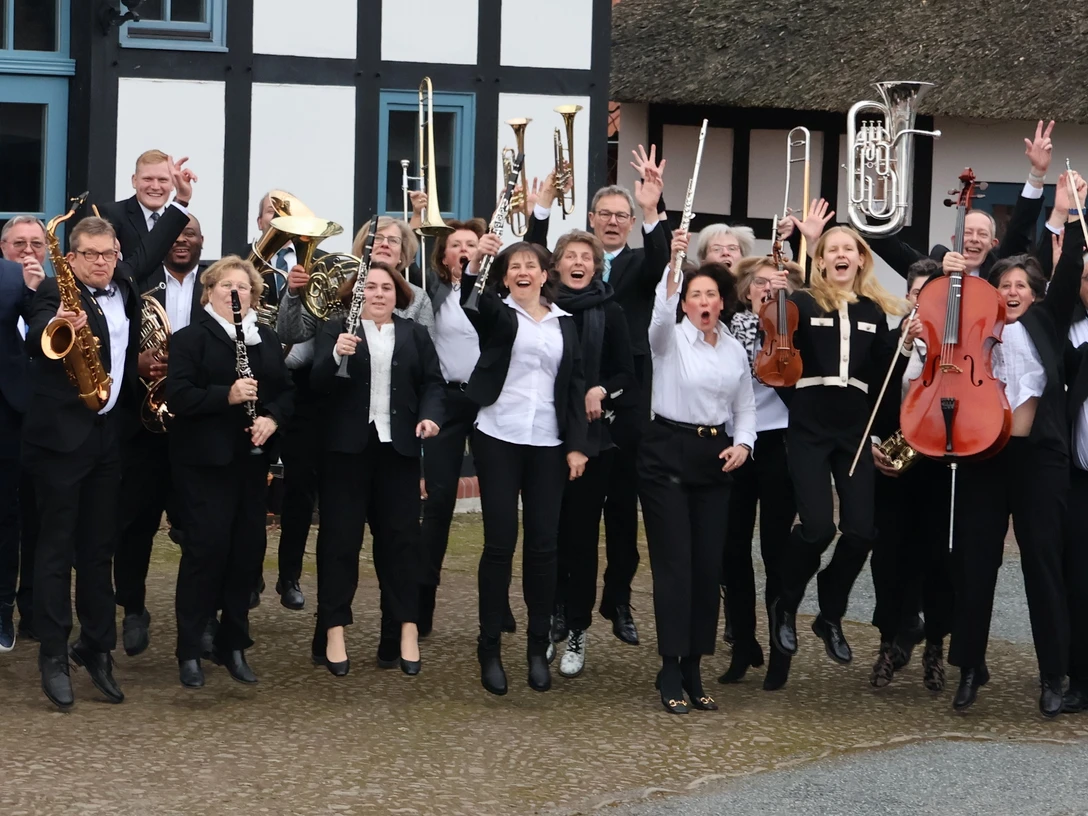 Musikverein Lemförde Musikergruppe springt vor Fachwerkhaus und hält verschiedene Instrumente in die Höhe