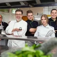 Wingst Hotel Peter, Küchenteam Fünfköpfiges Küchenteam im Genusshotel Peters Wingst lächelt gemeinsam in einer modernen Küche