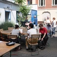 ehrenfeldstudios Personen in einem sonnigen Innenhof an Tischen im Gespräch und beim Vorbereiten einer AktivitätPeople in a sunny courtyard at tables talking and preparing an activity