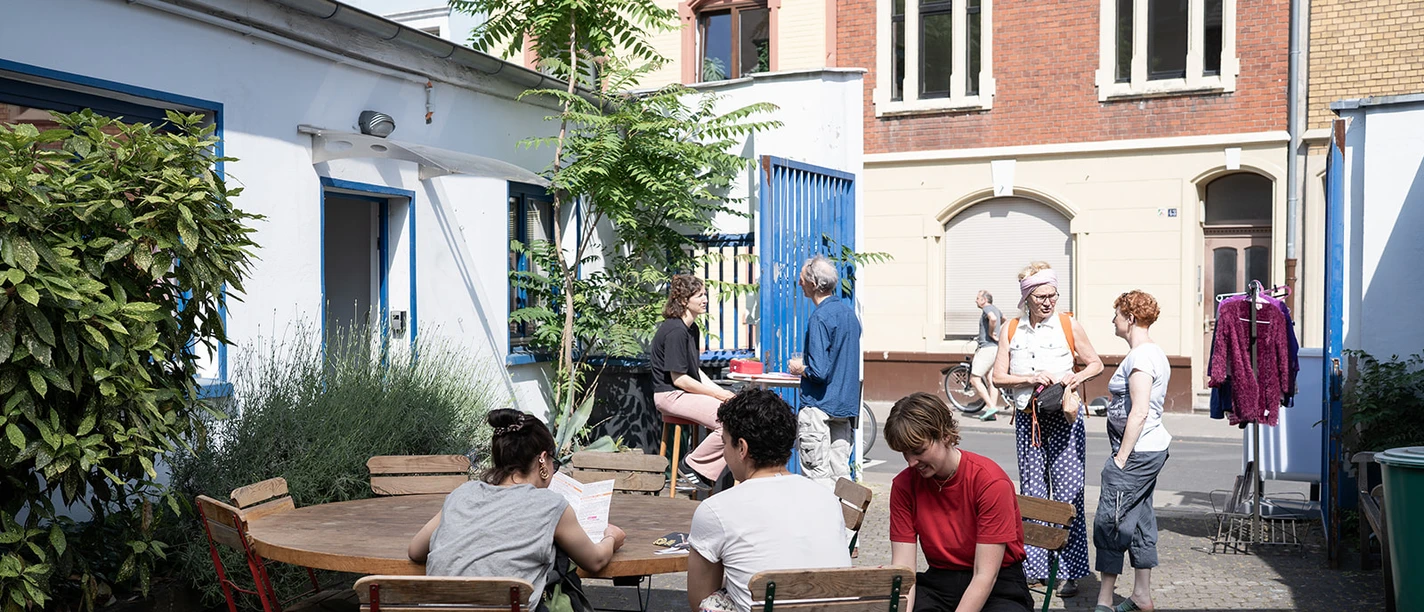 ehrenfeldstudios Personen in einem sonnigen Innenhof an Tischen im Gespräch und beim Vorbereiten einer Aktivität
